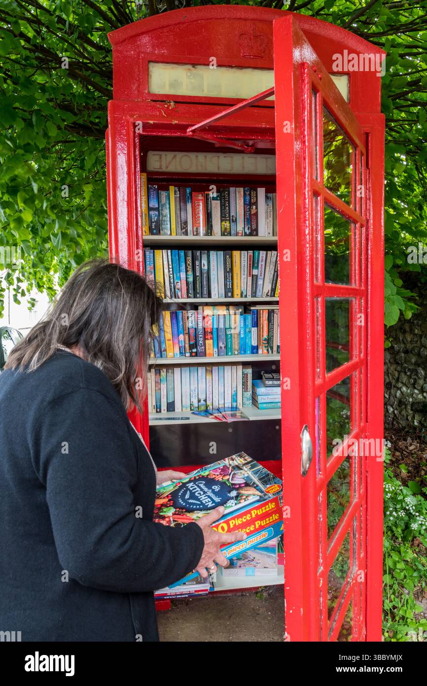 Donna che dona seghetti alternativi a una biblioteca di libri e seghetti in una scatola telefonica riutilizzata nel villaggio di Brancaster nel Norfolk settentrionale. Foto Stock