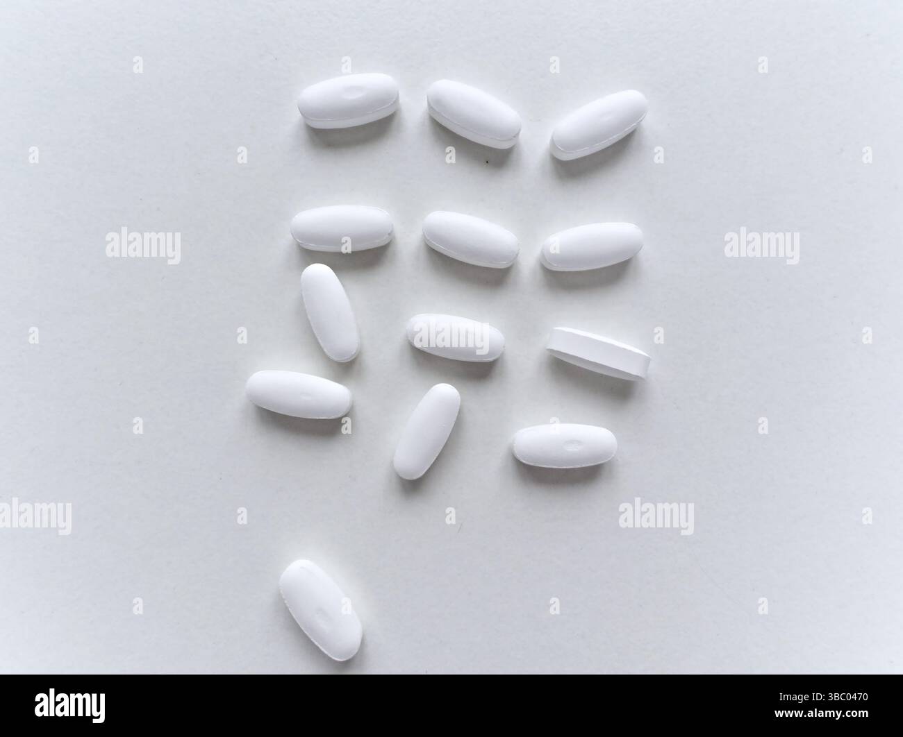 Una pillola bianca si trova su una superficie bianca. Ci sono molte pillole bianche sulla superficie. Le pillole sono tutte della stessa dimensione e forma Foto Stock