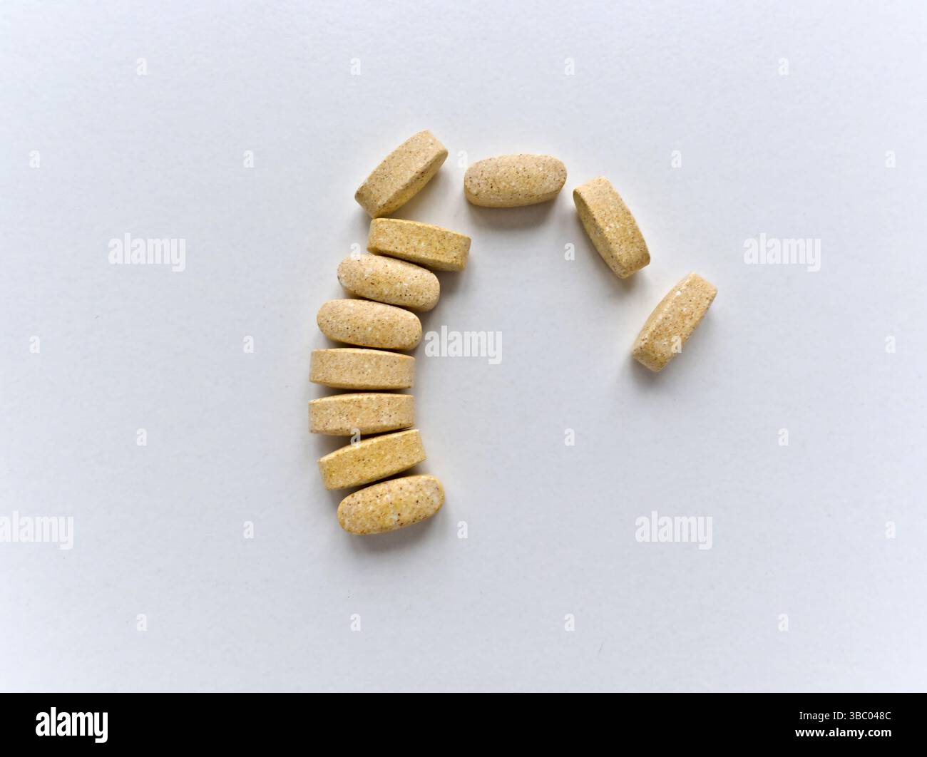 Una fila di pillole è disposta in una linea curva. Le pillole sono gialle e sembrano essere integratori vitaminici. Concetto di salute e benessere Foto Stock