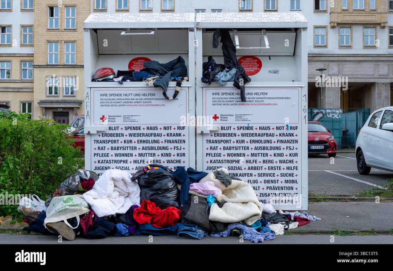 Bidoni per donazioni di abbigliamento traboccanti della Croce Rossa tedesca a Berlino, con indumenti impilati a terra intorno ai contenitori. Foto Stock