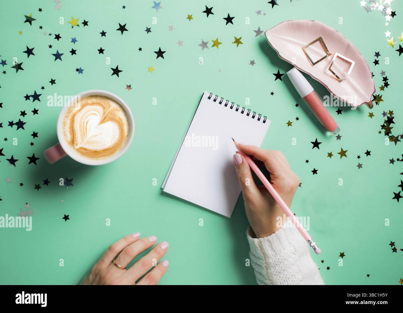 Le mani della donna in pullover bianco che fa piani per il prossimo anno, scrivendoli in notebook. Fare la lista dei desideri o il concetto di risoluzioni di Capodanno. Vista dall'alto, b Foto Stock