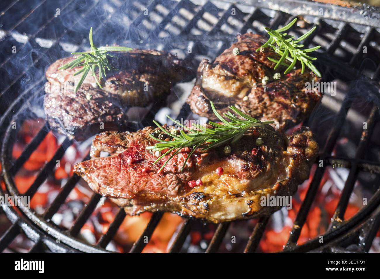 Guarnire la carne alla griglia con il rosmarino fresco. Utilizzando erbe aromatiche per rendere speciale la carne alla griglia. Primo piano carne cotta, barbecue fiamma sul dorso Foto Stock