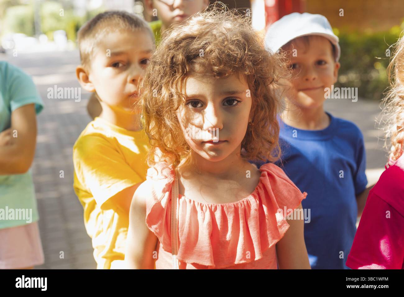 Ritratto di ragazza prescolare carina con capelli ricci, guardando tristemente la macchina fotografica. Ragazza insoddisfatta al campo estivo tra i suoi coetanei. Il volto della ragazza con l'ombra Foto Stock