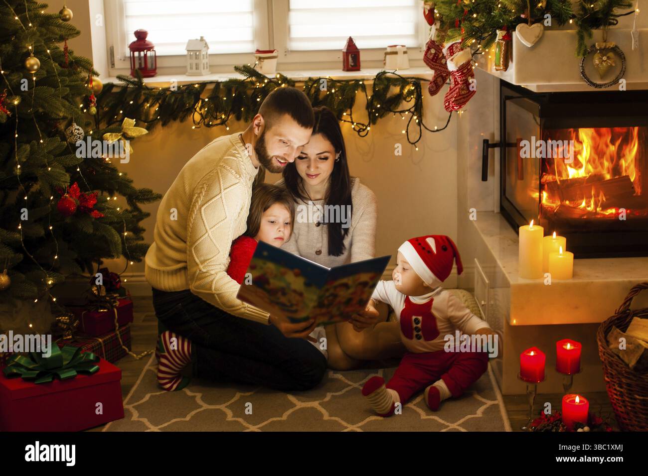 Felice famiglia che legge le favole di Natale. Tradizioni di famiglia di Natale. Interni moderni e festosi a casa a Christmastime Foto Stock