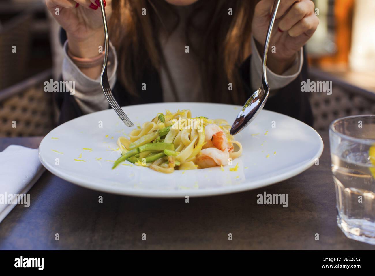 Primo piano di un piatto di fettuccine condito con gamberi. Donna che mangia al tavolo Foto Stock