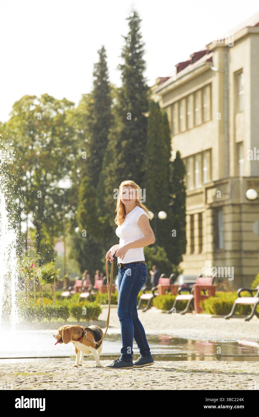 Una giovane donna che cammina con un cane da aquila su un guinzaglio vicino alla fontana nel parco Foto Stock