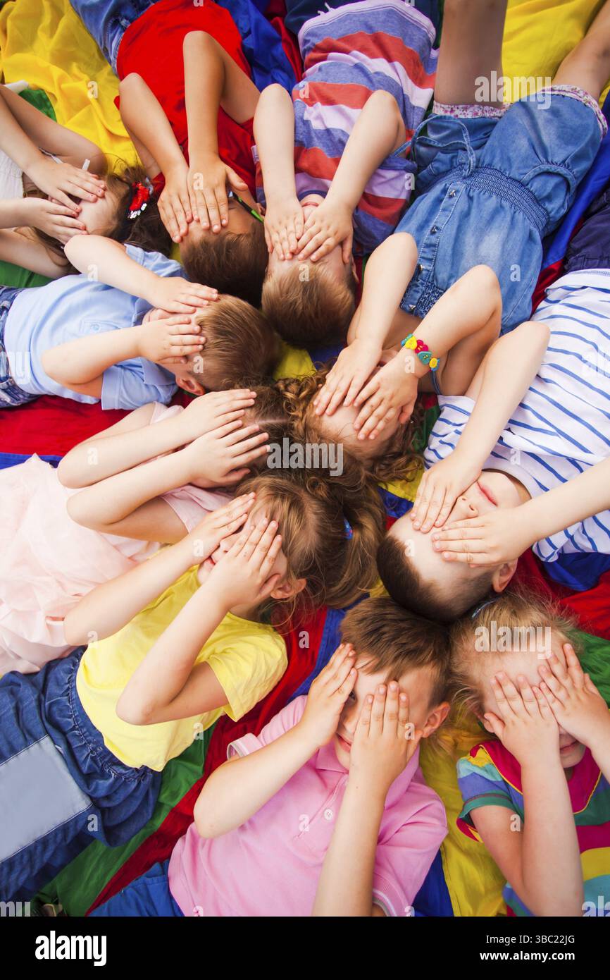 I bambini si rilassano su un pavimento mentre si rompono, posando le facce coprenti con le mani. Bambini che lavorano sulle tecniche di rilassamento. Campo estivo. Pericolo di ped Foto Stock