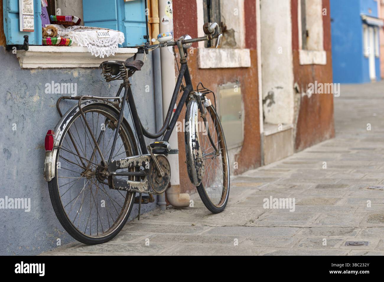 Una vecchia bicicletta si appoggia su una colorata facciata della casa su ciottoli, immagine simbolica, Burano, Venezia, Veneto, Italia, Europa Foto Stock