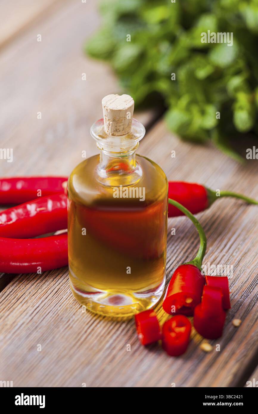 Il bicchiere di olio essenziale e fette di peperoncino su un tavolo di legno si chiudono Foto Stock