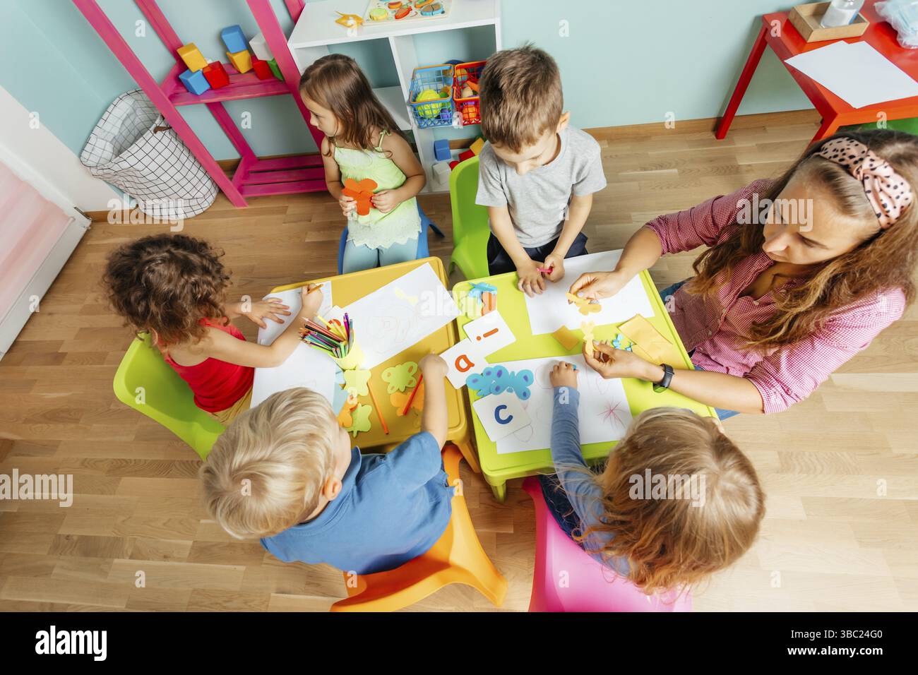 Ritratto di una bella ragazza riccia seduta, con un grande foglio di carta, che mostra il suo disegno alla fotocamera. Lezione d'arte all'asilo o all'asilo. Sentire Foto Stock