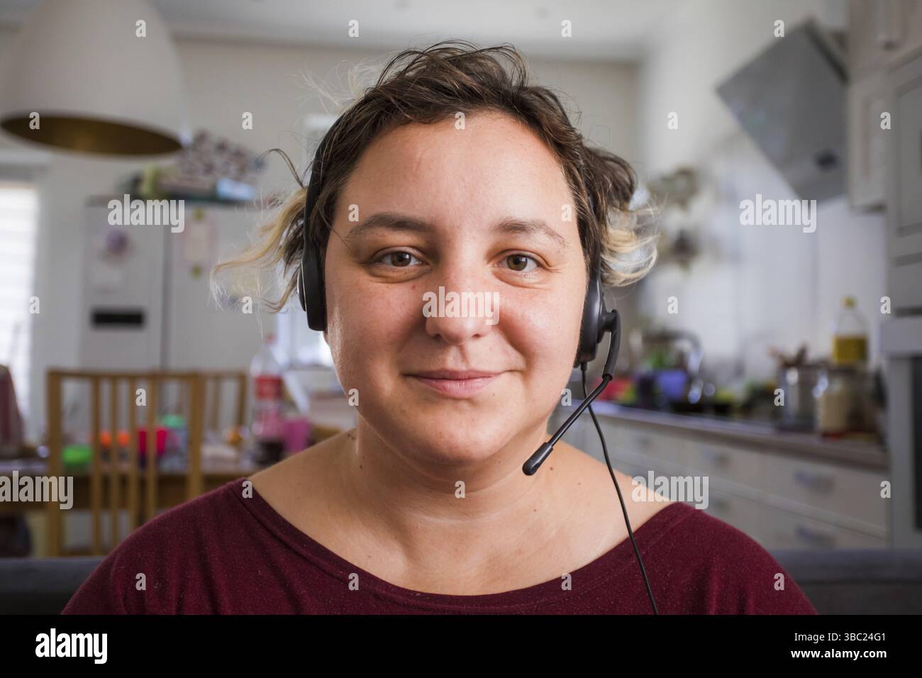 Ritratto di giovane donna attraente in cuffie durante la sua conference call. Insegnante che fornisce lezioni online durante la quarantena. Effetto di ripresa con la webcam Foto Stock