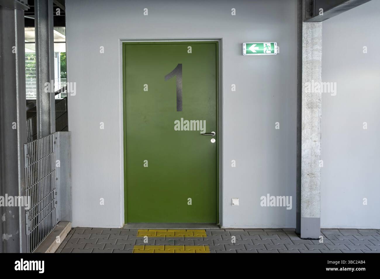 Porta numero uno dell'uscita antincendio verde con un cartello illuminato che mostra la via di fuga e la pavimentazione tattile, in un edificio moderno Foto Stock