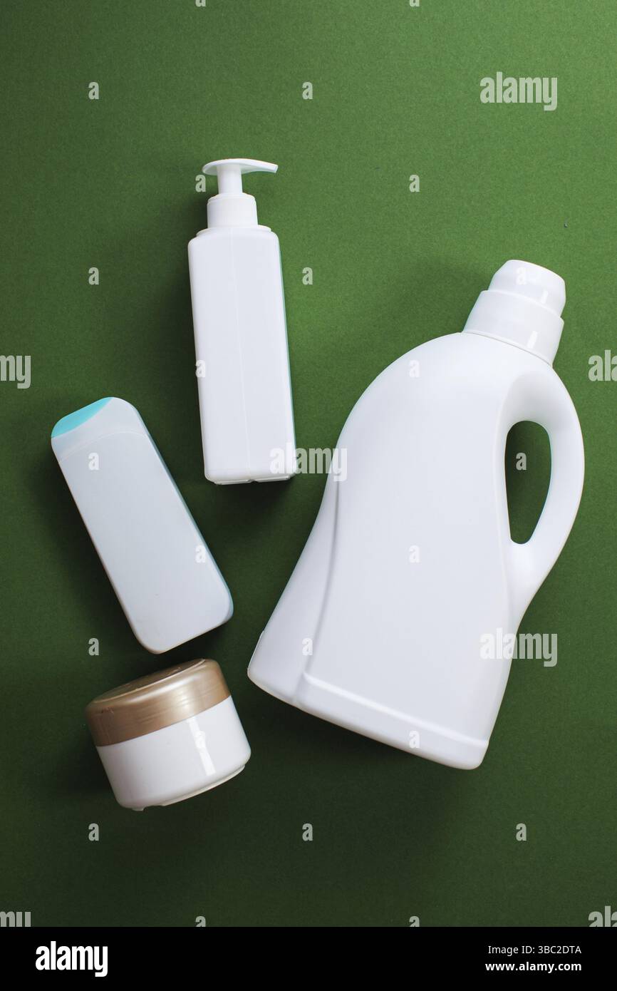 Prodotti chimici domestici o detersivo liquido per bucato e altro detergente su sfondo verde, vista dall'alto, piatto. Bottiglie di plastica bianche di prodotto detergente Foto Stock