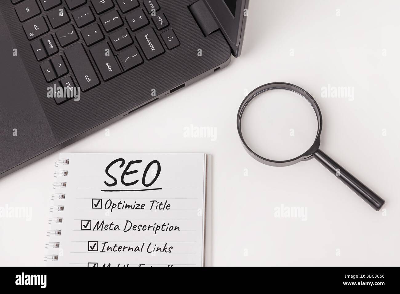 Un blocco note con lista di controllo SEO, un notebook nero, una lente di ingrandimento isolata su una scrivania bianca, che suggerisce attività di ottimizzazione e strategie per il miglioramento Foto Stock