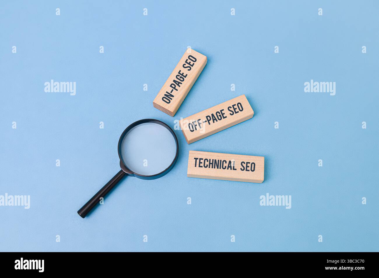 "Tre blocchi di legno etichettati "SEO on-page", "SEO off-page", "SEO tecnico" accanto a una lente di ingrandimento che concentra la parola "SEO" su sfondo blu. Foto Stock