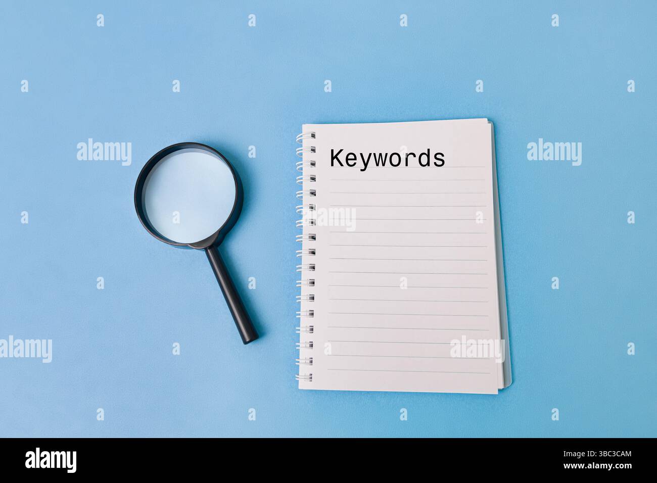 Accanto a un blocco note è posizionata una lente di ingrandimento con la parola "parole chiave" visualizzata in modo prominente. Ciò evidenzia l'importanza della ricerca per parole chiave in vari settori Foto Stock