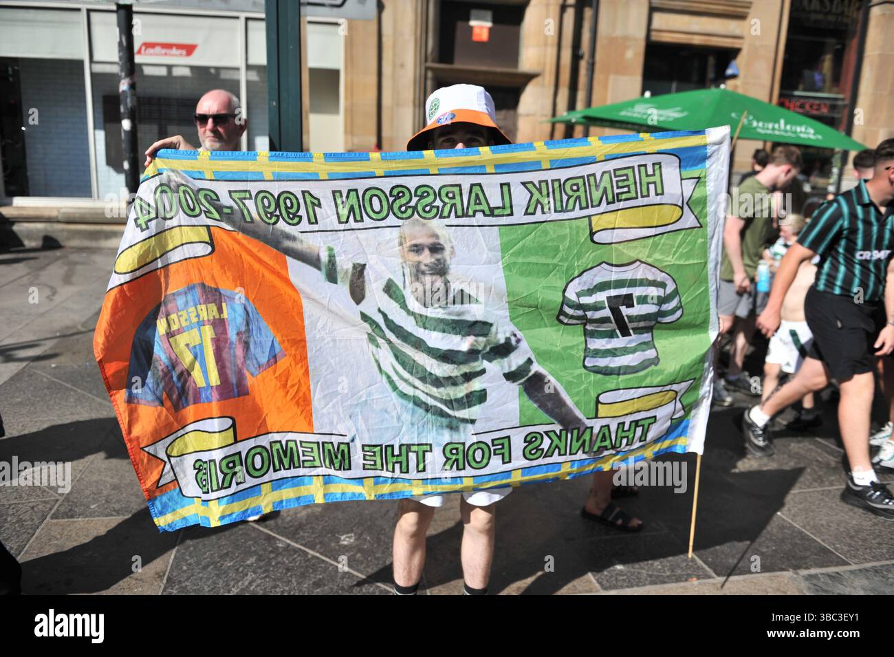 Glasgow, Regno Unito. 17 maggio 2025 - il fan è visto posare per i fotografi durante i festeggiamenti mentre tiene in mano una bandiera dell'ex giocatore Henrik Larsson, ringraziandoli per il loro tempo con il club. I tifosi del Celtic si sono riuniti nel centro di Glasgow il 17 maggio per celebrare la vittoria della Scottish Premiership dopo la vittoria della squadra. I sostenitori hanno allagato le aree della città Mercantile e di Trongate in uno spettacolo di festa vivace ma tranquillo. Crediti: Eastern Goodwin Media/Alamy Live News Foto Stock Glasgow, Regno Unito. 17 maggio 2025 - il fan è visto posare per i fotografi durante i festeggiamenti mentre tiene in mano una bandiera dell'ex giocatore Henrik Larsson, ringraziandoli per il loro tempo con il club. I tifosi del Celtic si sono riuniti nel centro di Glasgow il 17 maggio per celebrare la vittoria della Scottish Premiership dopo la vittoria della squadra. I sostenitori hanno allagato le aree della città Mercantile e di Trongate in uno spettacolo di festa vivace ma tranquillo. Crediti: Eastern Goodwin Media/Alamy Live News Foto Stock
