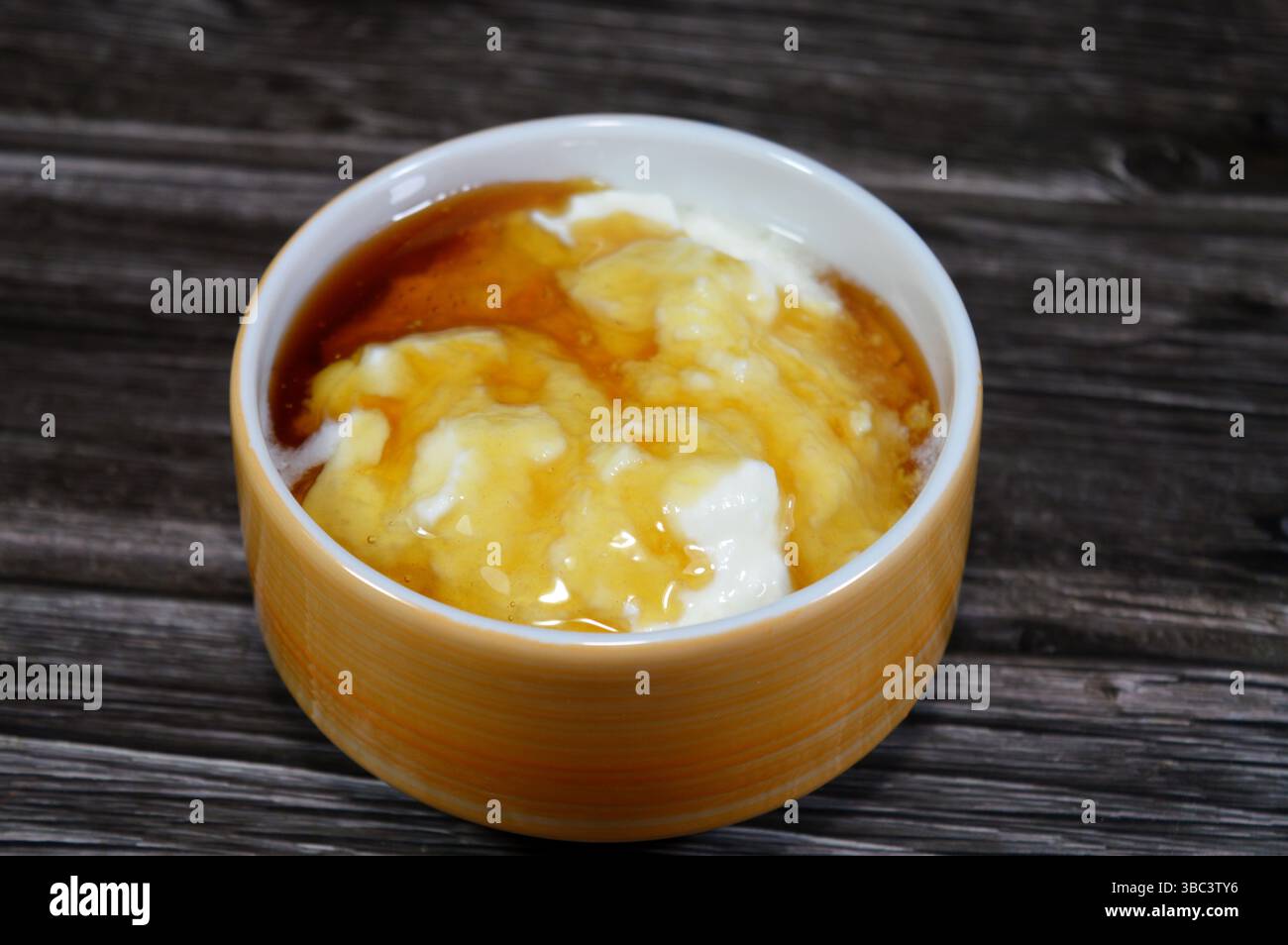 Il miele sopra lo yogurt naturale, un alimento prodotto dalla fermentazione batterica del latte, la fermentazione degli zuccheri nel latte da parte di questi batteri produce lacti Foto Stock