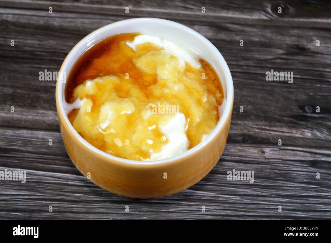 Il miele sopra lo yogurt naturale, un alimento prodotto dalla fermentazione batterica del latte, la fermentazione degli zuccheri nel latte da parte di questi batteri produce lacti Foto Stock