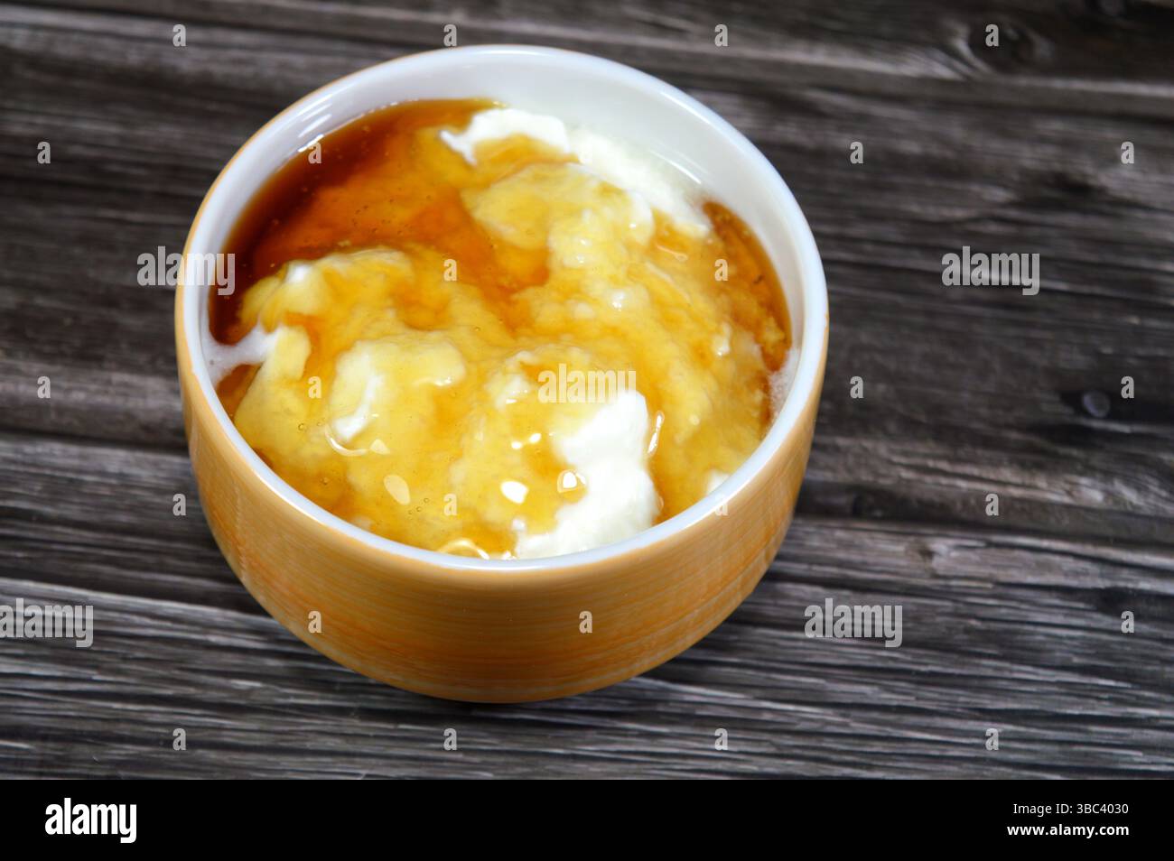 Il miele sopra lo yogurt naturale, un alimento prodotto dalla fermentazione batterica del latte, la fermentazione degli zuccheri nel latte da parte di questi batteri produce lacti Foto Stock