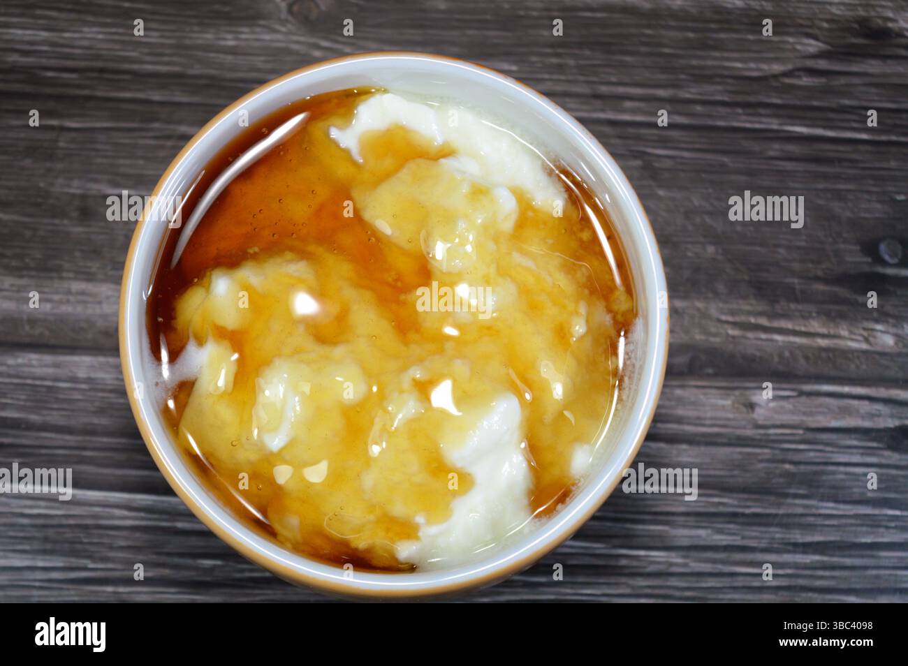 Il miele sopra lo yogurt naturale, un alimento prodotto dalla fermentazione batterica del latte, la fermentazione degli zuccheri nel latte da parte di questi batteri produce lacti Foto Stock