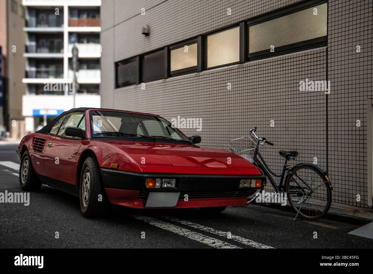 Classica Ferrari Mondial rossa parcheggiata accanto a una bicicletta in un tranquillo vicolo di Tokyo, evidenziando il contrasto tra lusso e semplicità Foto Stock