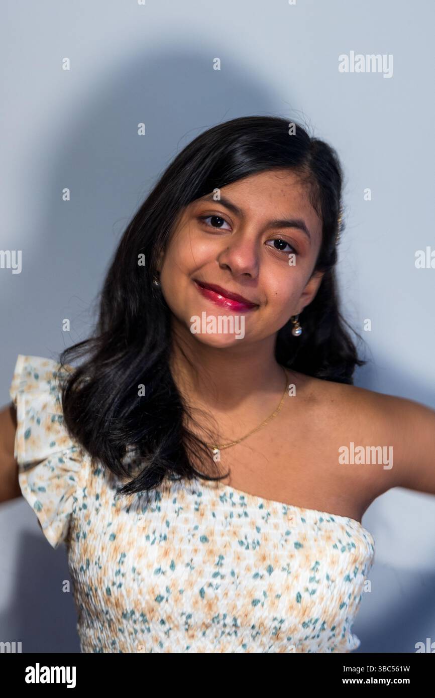 Una giovane donna indossa un abito floreale bianco e giallo e sorride. Sta potendo per un film Foto Stock