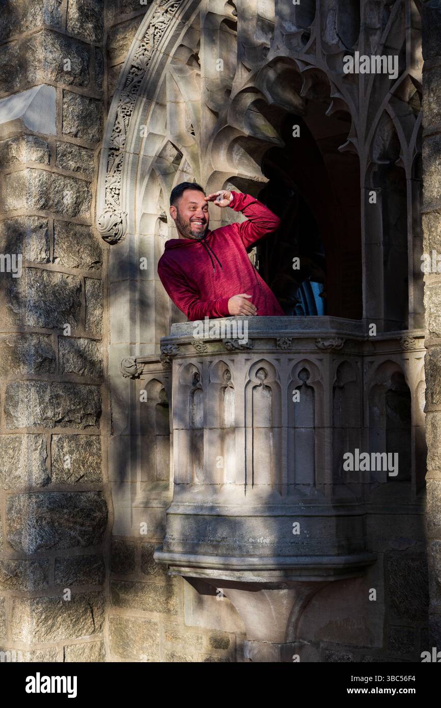 Un uomo con una felpa con cappuccio rossa guarda fuori dalla finestra. La scena è spensierata e giocosa Foto Stock Un uomo con una felpa con cappuccio rossa guarda fuori dalla finestra. La scena è spensierata e giocosa Foto Stock