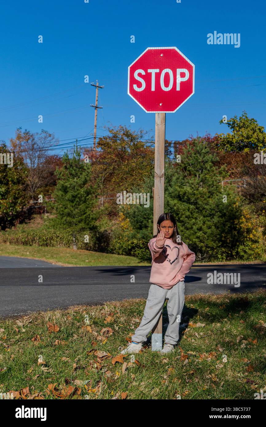 Una ragazza è in piedi davanti a un segnale di stop. Indossa un maglione rosa e pantaloni grigi Foto Stock