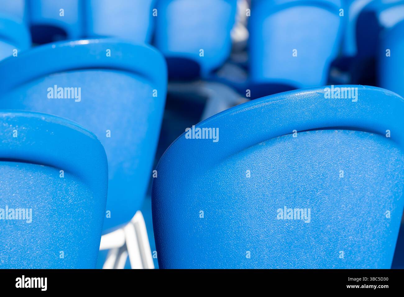 Primo piano luminoso di più sedie in plastica blu in una disposizione ordinata, che enfatizza la struttura e il design, trasmettendo estetica e funzionalità Foto Stock