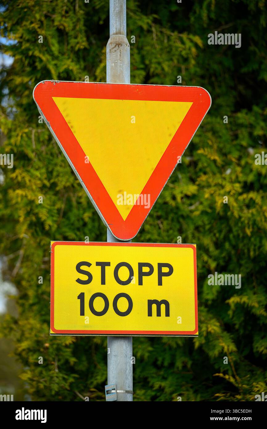 Un segnale stradale triangolare rosso e giallo indica al conducente di cedere, mentre un altro segnale in grassetto mostra un segnale di stop entro 100 metri. Il retro Foto Stock