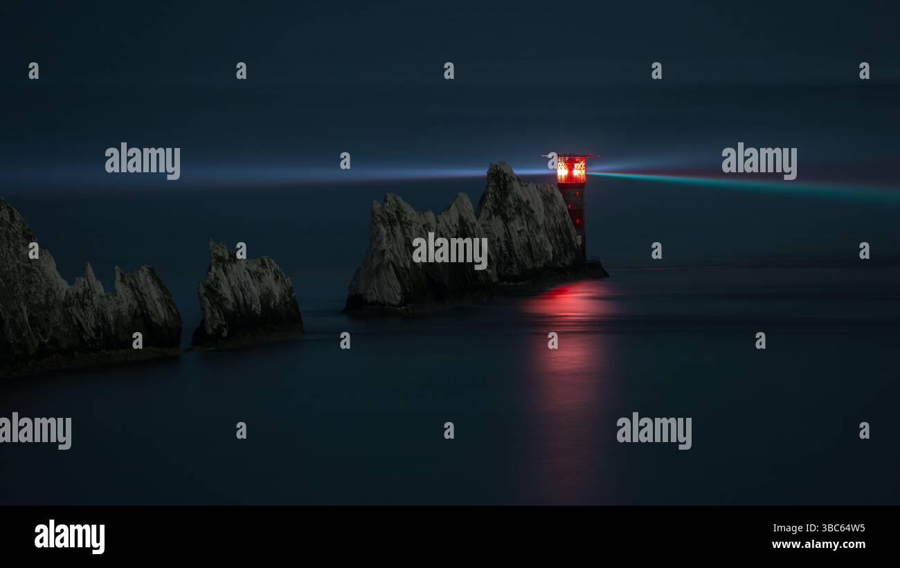 Il faro di Needles sull'isola di Wight di notte, con un settore luminoso rosso che splende attraverso la nebbia. Esposizione lunga che mostra un fascio di luce sul mare calmo. Foto Stock