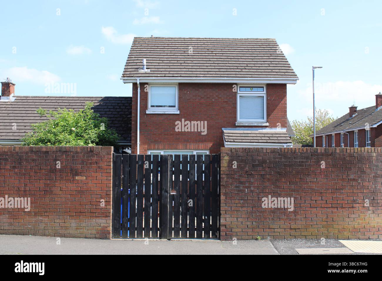 Muro della pace dell'epoca dei problemi di fronte a una casa di mattoni a Belfast, Irlanda del Nord Foto Stock