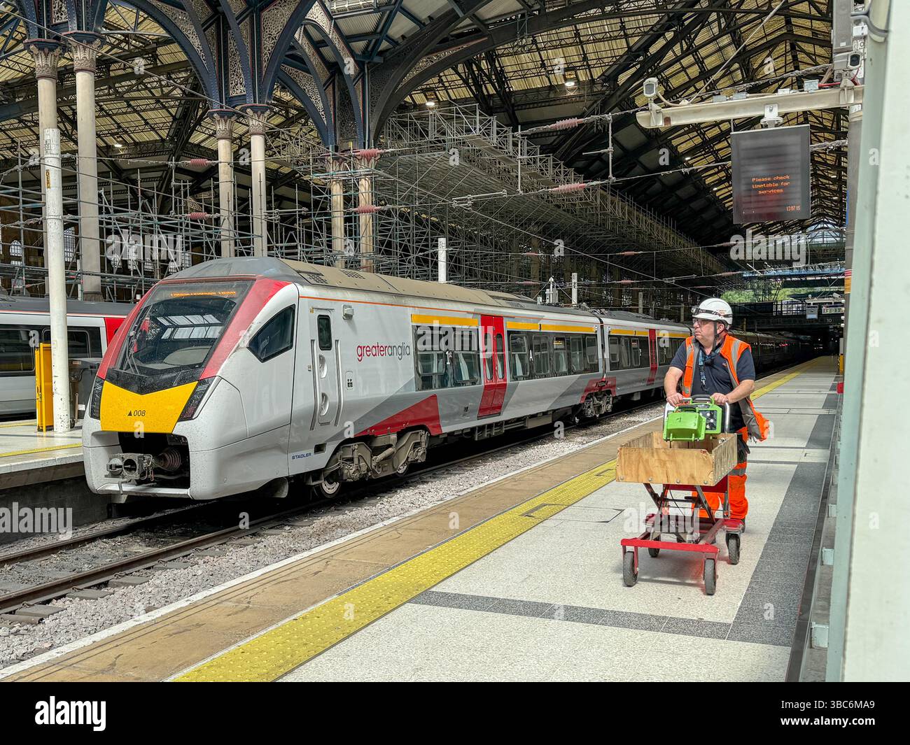 Un ingegnere spinge un carrello da lavoro lungo la piattaforma alla stazione di Liverpool Street, di fronte a un treno Great Anglia che si prepara a partire dal Regno Unito DA LONDRA Foto Stock