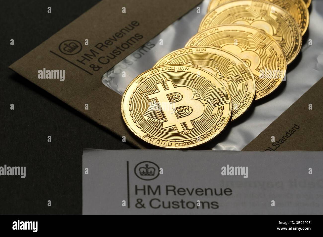 Stack di monete Bitcoin che emergono dalla busta HM Revenue & Customs, simboleggiando la tassazione delle criptovalute e la regolamentazione finanziaria nel Regno Unito, Stafford, Foto Stock
