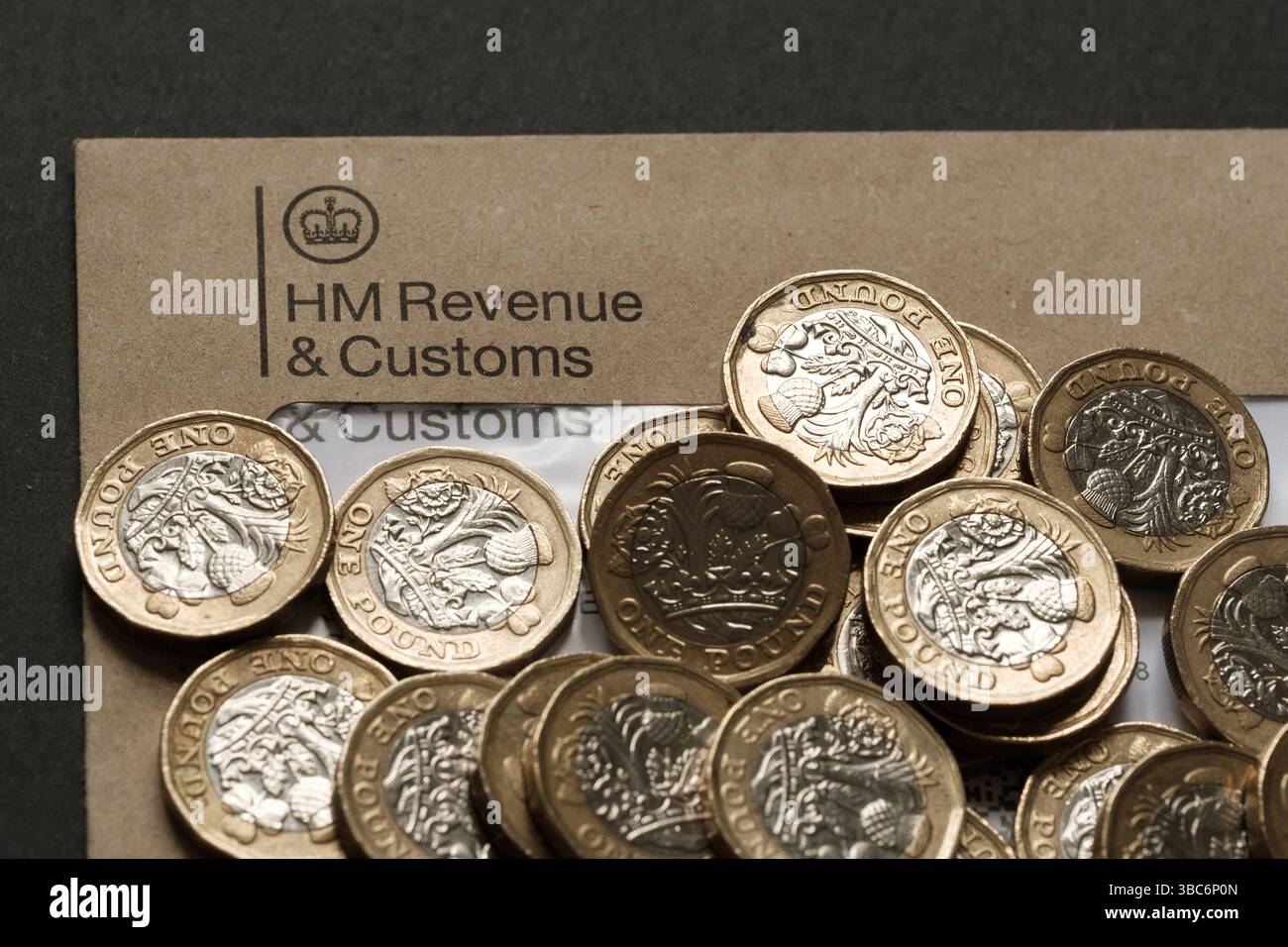 Primo piano di monete inglesi da una sterlina sparse sulla busta HM Revenue & Customs, che rappresenta la tassazione personale e la responsabilità finanziaria, Staffor Foto Stock