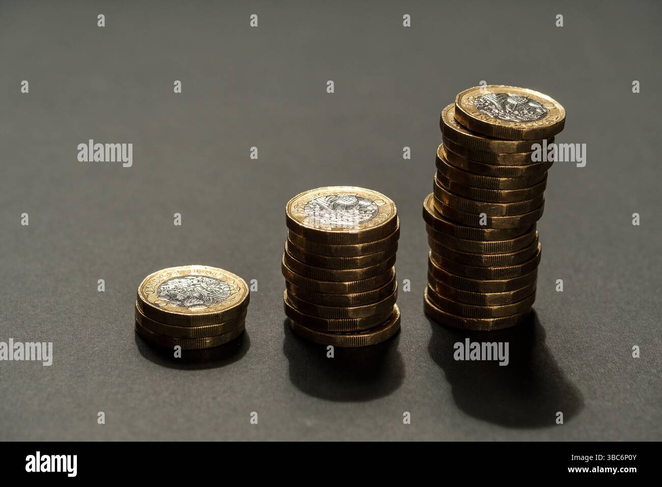 Tre pile ascendenti di monete inglesi da una sterlina disposte su una superficie scura, simboleggiando la crescita finanziaria, il risparmio e la progressione economica, Staffor Foto Stock