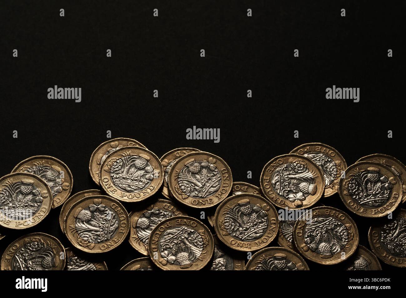 Monete britanniche sparse da una sterlina lungo il bordo inferiore di uno sfondo nero, che rappresentano risparmi, guadagni e valuta del Regno Unito, Stafford, Regno Unito Foto Stock