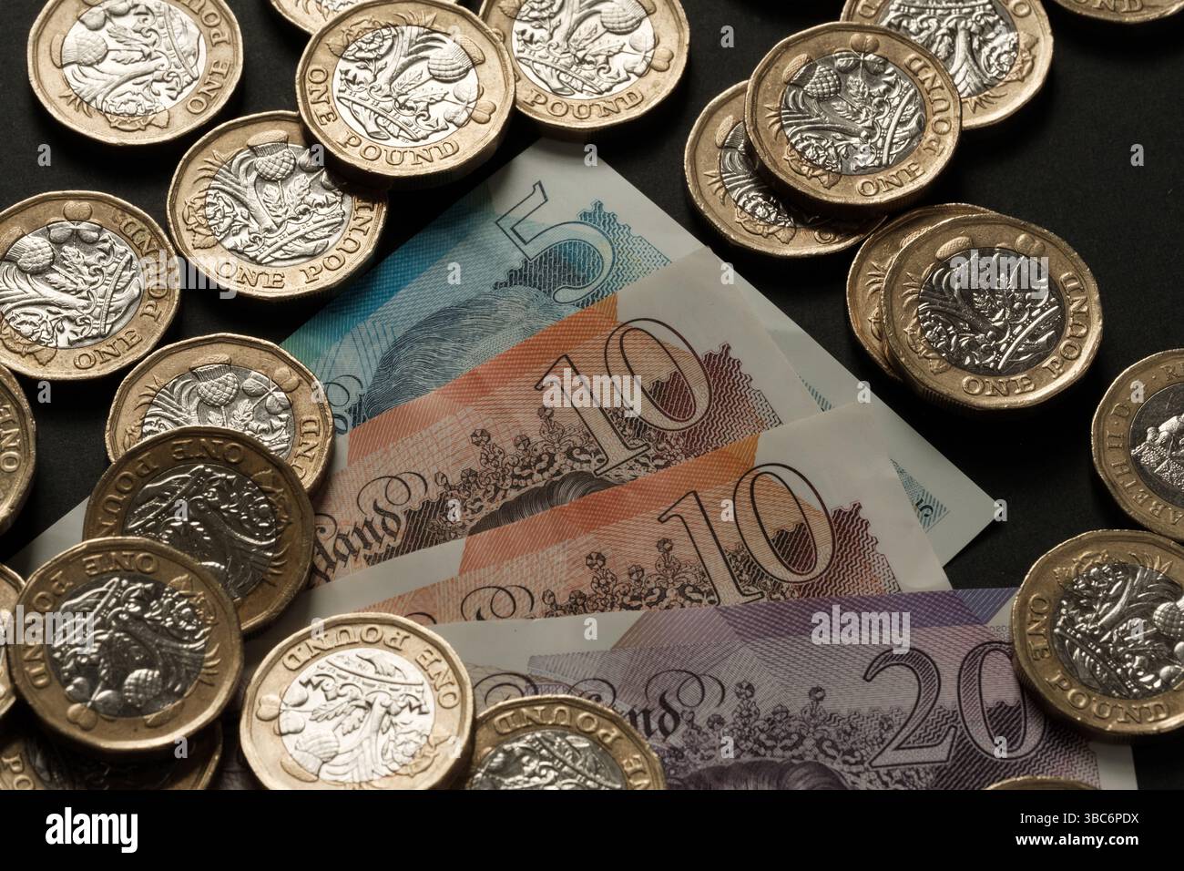 Banconote britanniche e monete da una sterlina sparse su una superficie scura, che rappresentano la valuta del Regno Unito, il flusso di cassa e la ricchezza finanziaria, Stafford, Regno Unito Foto Stock