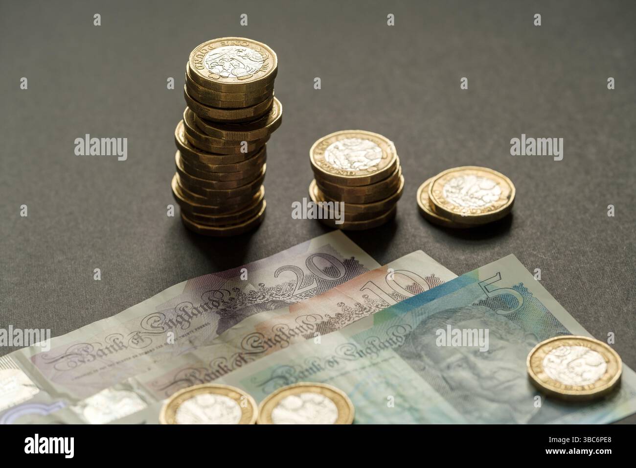 Pile di monete inglesi da una sterlina disposte in altezza decente accanto a banconote da 5, 10 e 20, simboleggiando lo stato finanziario e il risparmio, Stafford, United Foto Stock