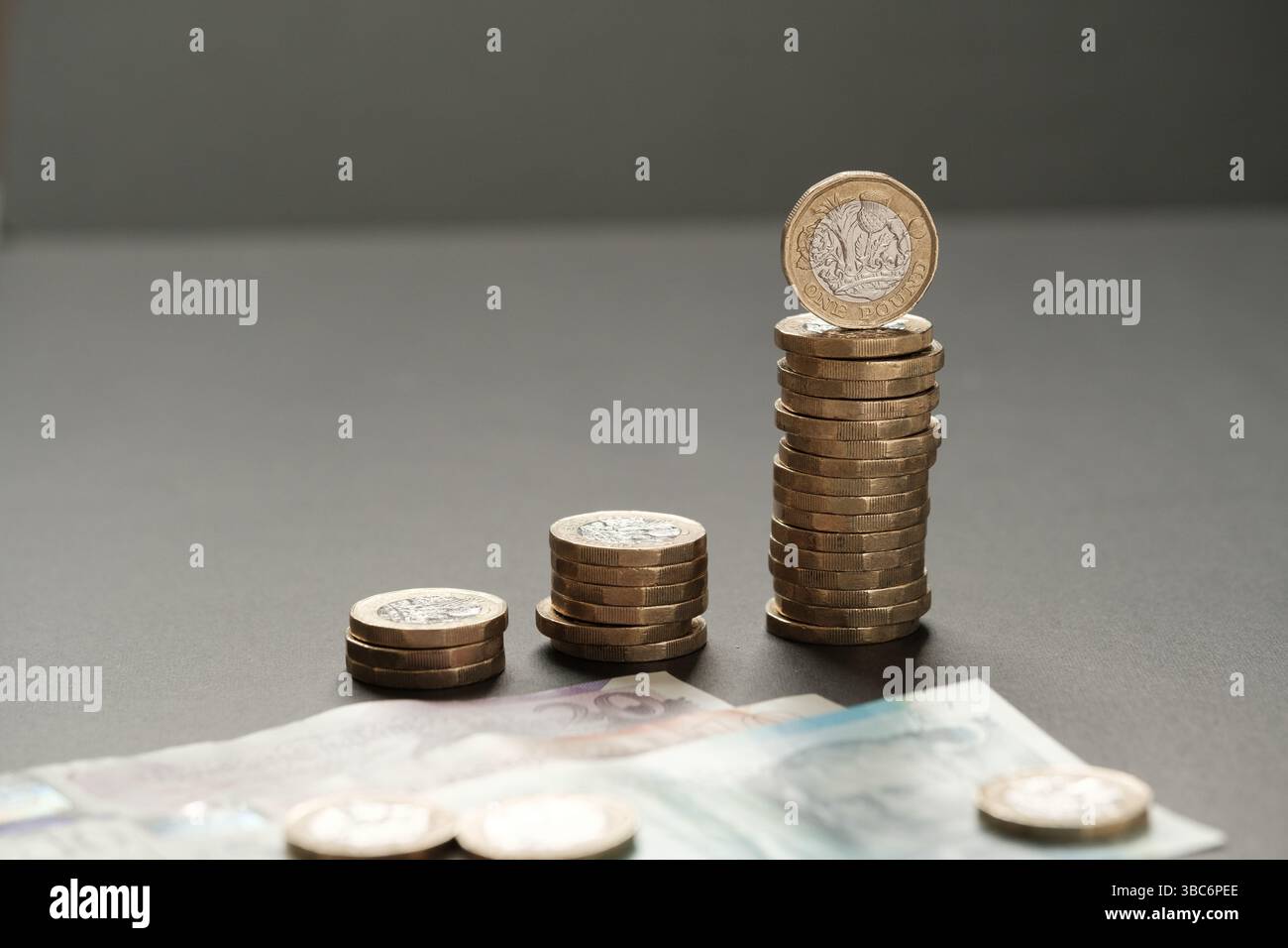 Pile crescenti di monete da una sterlina collocate sopra le banconote da cinque, dieci e venti sterline su una superficie scura, simboleggiando la crescita finanziaria e gli incrementi di reddito Foto Stock