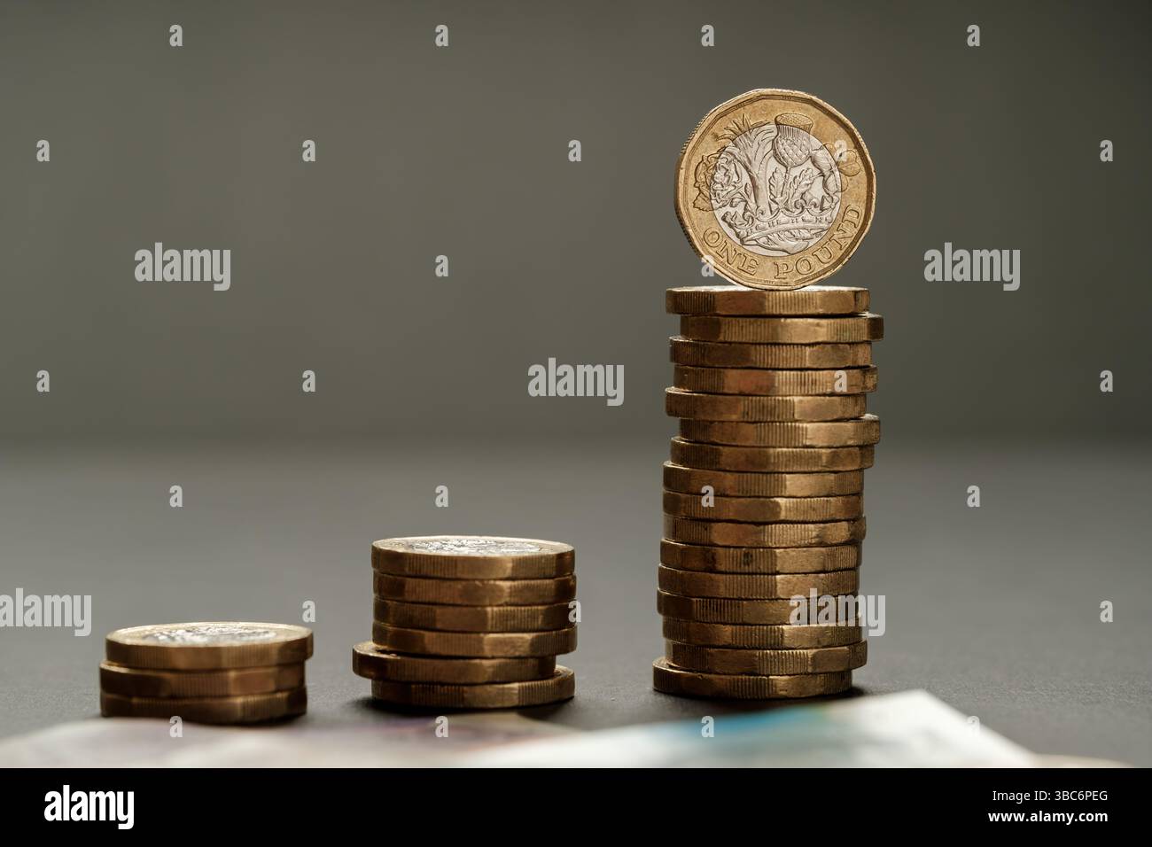 Tre pile crescenti di monete da una sterlina disposte in ordine ascendente con banconote sfocate in primo piano, illustrando la crescita del reddito e finanziaria Foto Stock