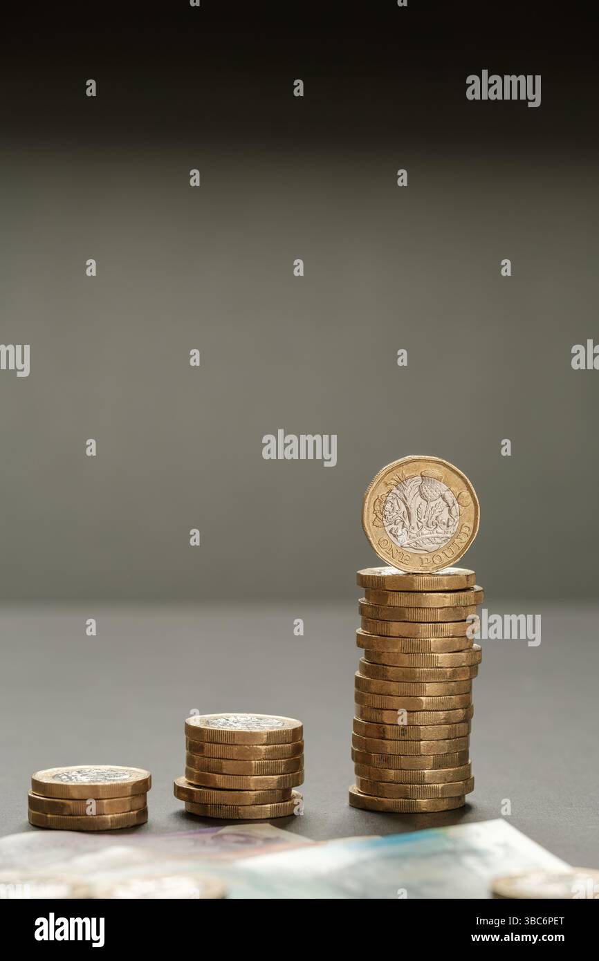 Immagine verticale di monete da una sterlina impilate che formano un grafico a barre in aumento con le banconote britanniche in primo piano, simboleggiando la crescita del reddito e la suc finanziaria Foto Stock