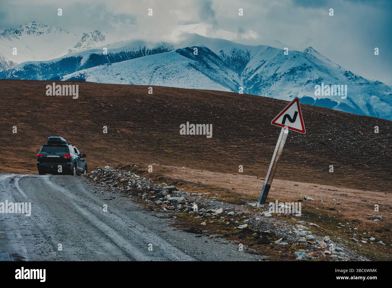 Auto da viaggio e segnale di svolta pericolosa sulla strada di montagna Foto Stock