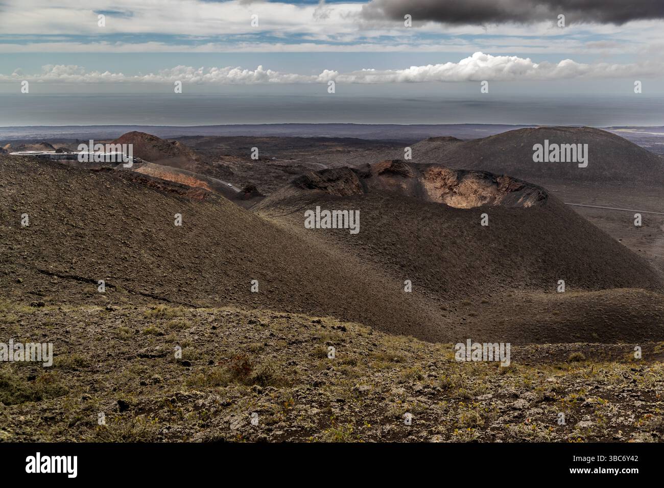 Terreno vulcanico su Lanzarote con il centro informazioni Islote de Hilario - Parque Nacional de Timanfaya su un cratere. Camino pista Rural Ruta de los Volcanes, Yaiza, Lanzarote, Isole Canarie, Spagna Foto Stock