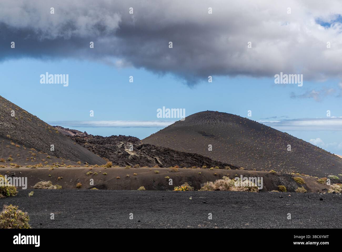 Un cono vulcanico simmetrico si erge sopra il campo di lava nell'area vulcanica vicino a Mancha Blanca a Lanzarote. Nuvole scure incombono sul paesaggio sterile. Isole Canarie, Spagna. Foto Stock