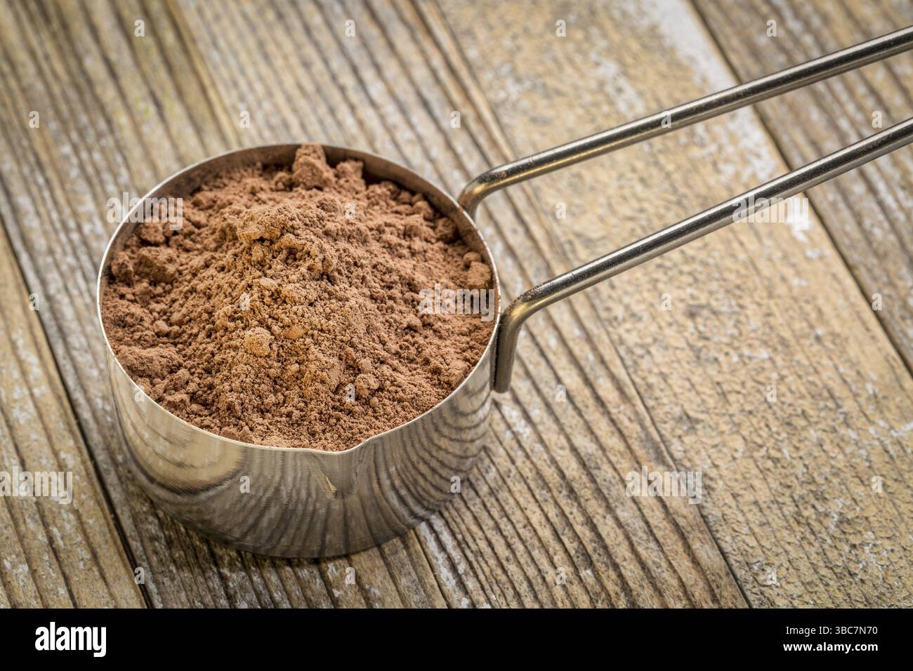 Polvere di cacao in un misurino metallico su fondo in legno grunge Foto Stock