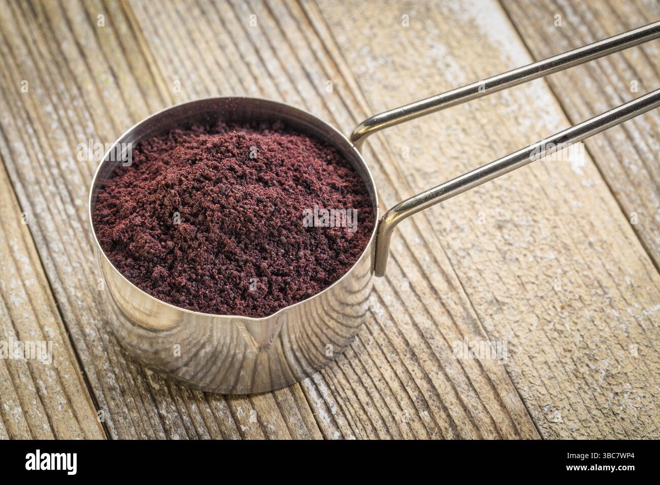 Polvere di bacca di acai in un misurino metallico su fondo in legno grunge Foto Stock