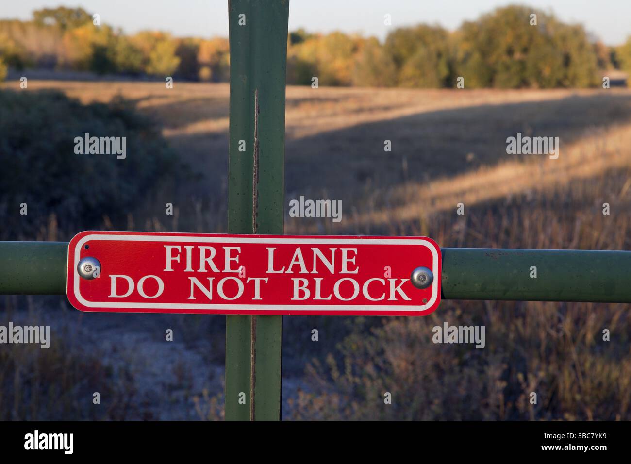 Fire Lane, non bloccare il cartello su un cancello con un prato e un paesaggio boschivo alle spalle Foto Stock