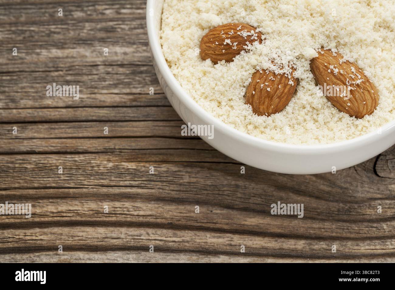Farina di mandorle ad alto contenuto di proteine, basso contenuto di carboidrati, basso contenuto di zuccheri e senza glutine - una ciotola in ceramica su fondo in legno granulare Foto Stock